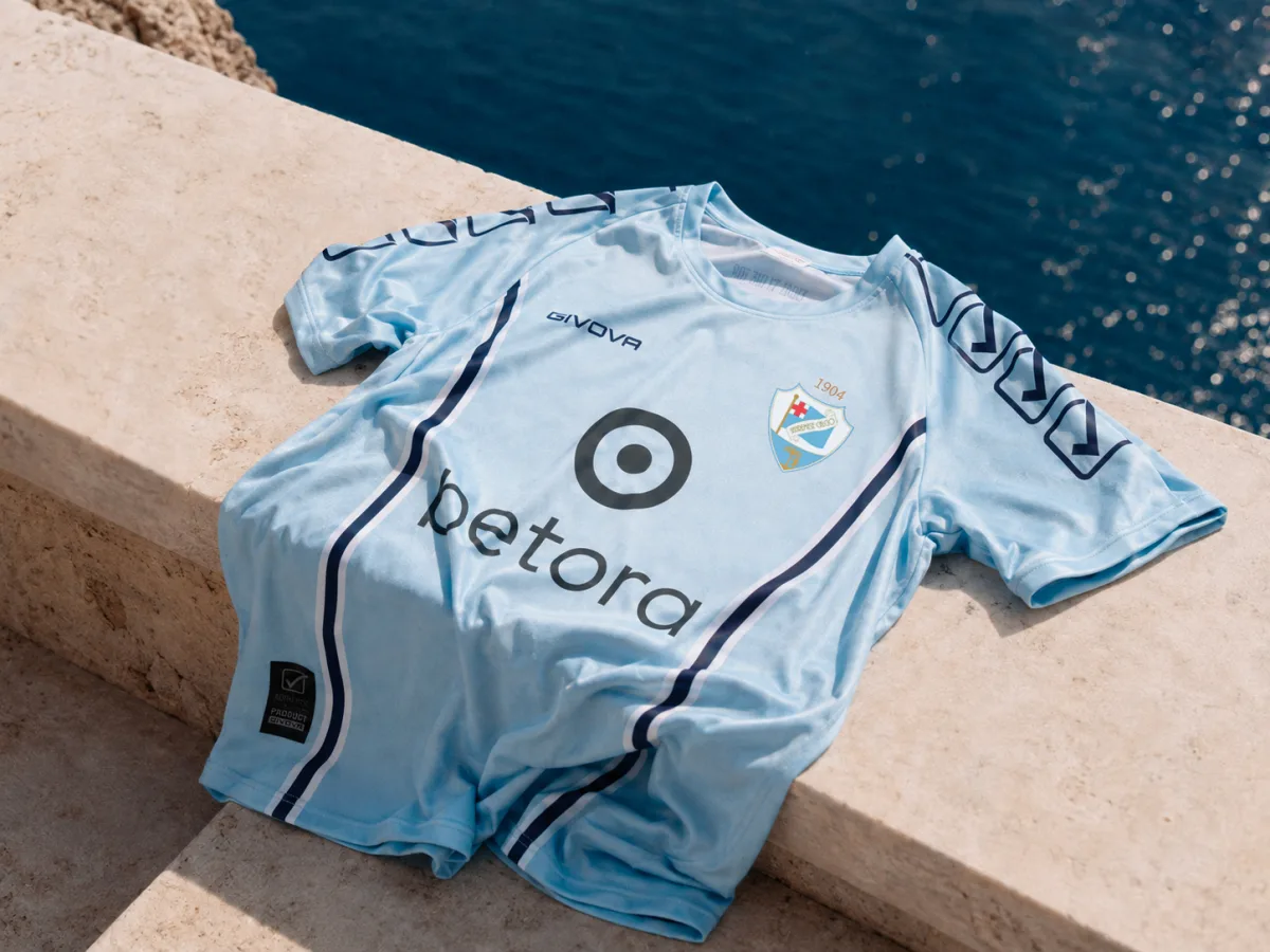 Maglia Home 2026/27 della Sanremese Calcio, azzurra, appoggiata su un muretto davanti al mare